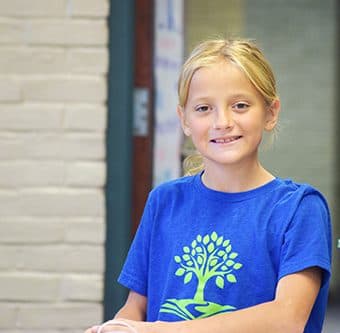 A smiling New Richmond Prep student in a blue school shirt.