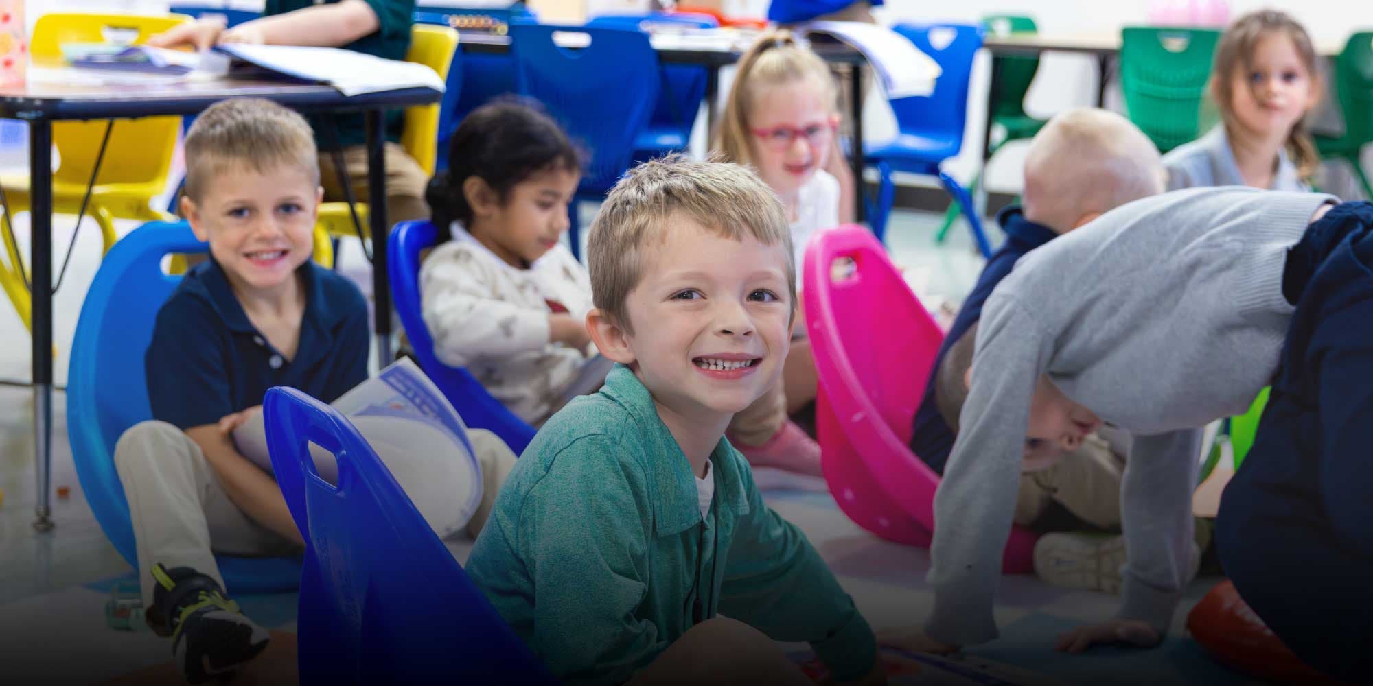 Smiling student sitting on a floor seat with classmates in a classroom.