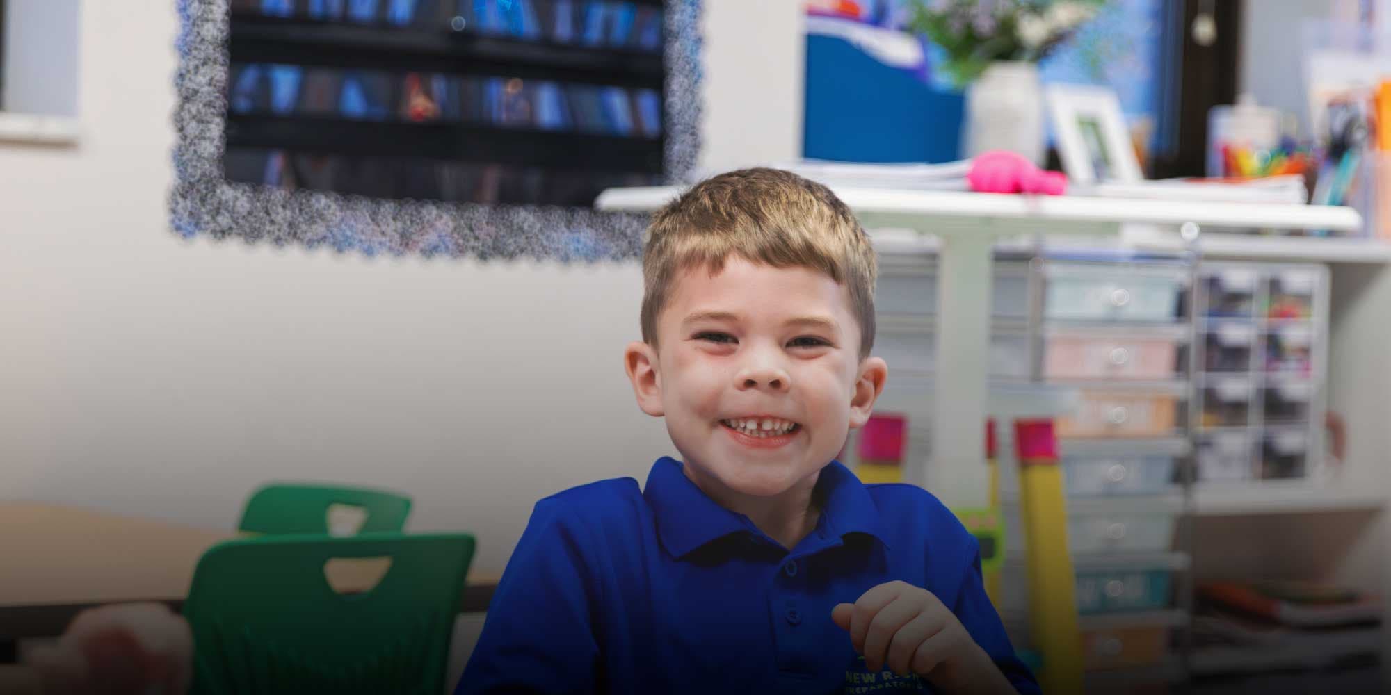 Smiling student in a blue school polo in a classroom.