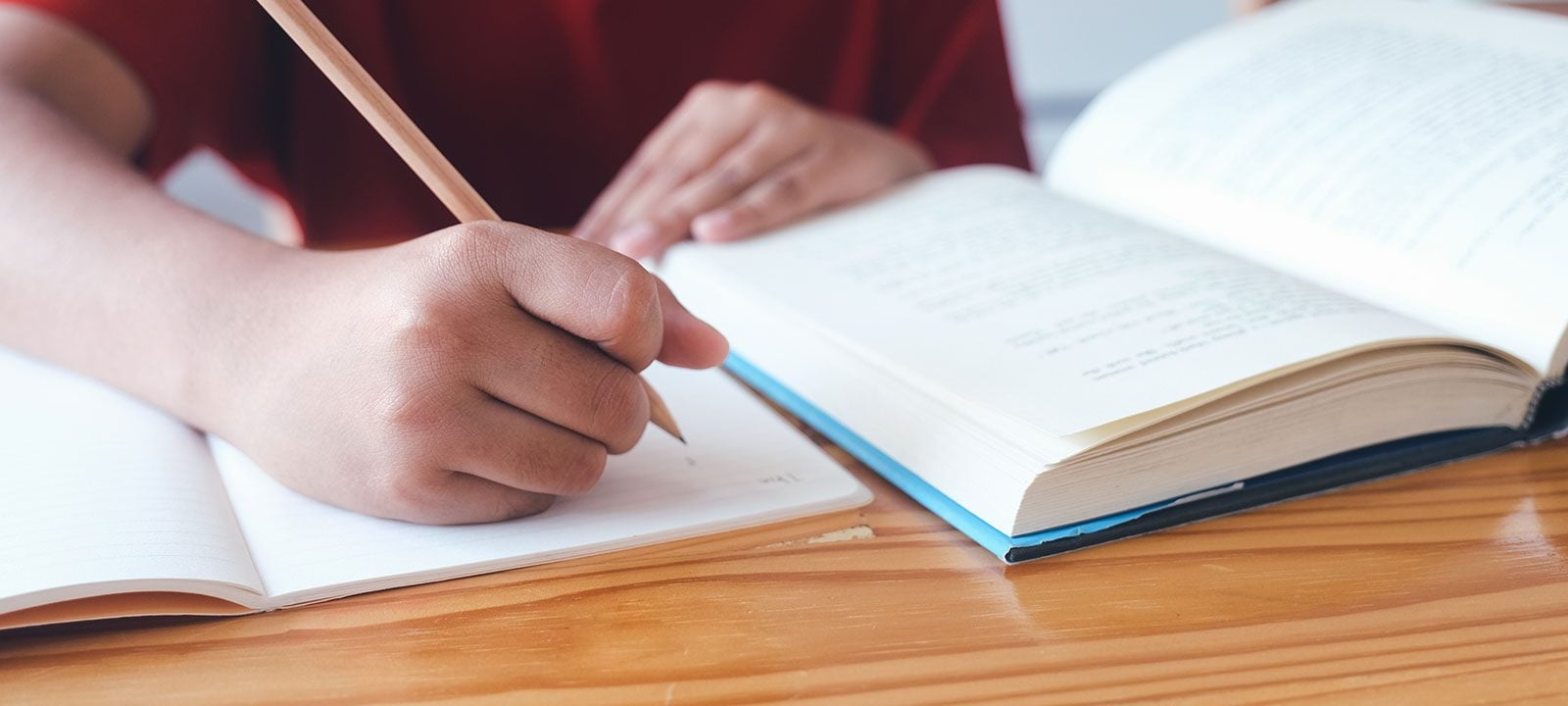 Person writing in a notebook next to an open book.